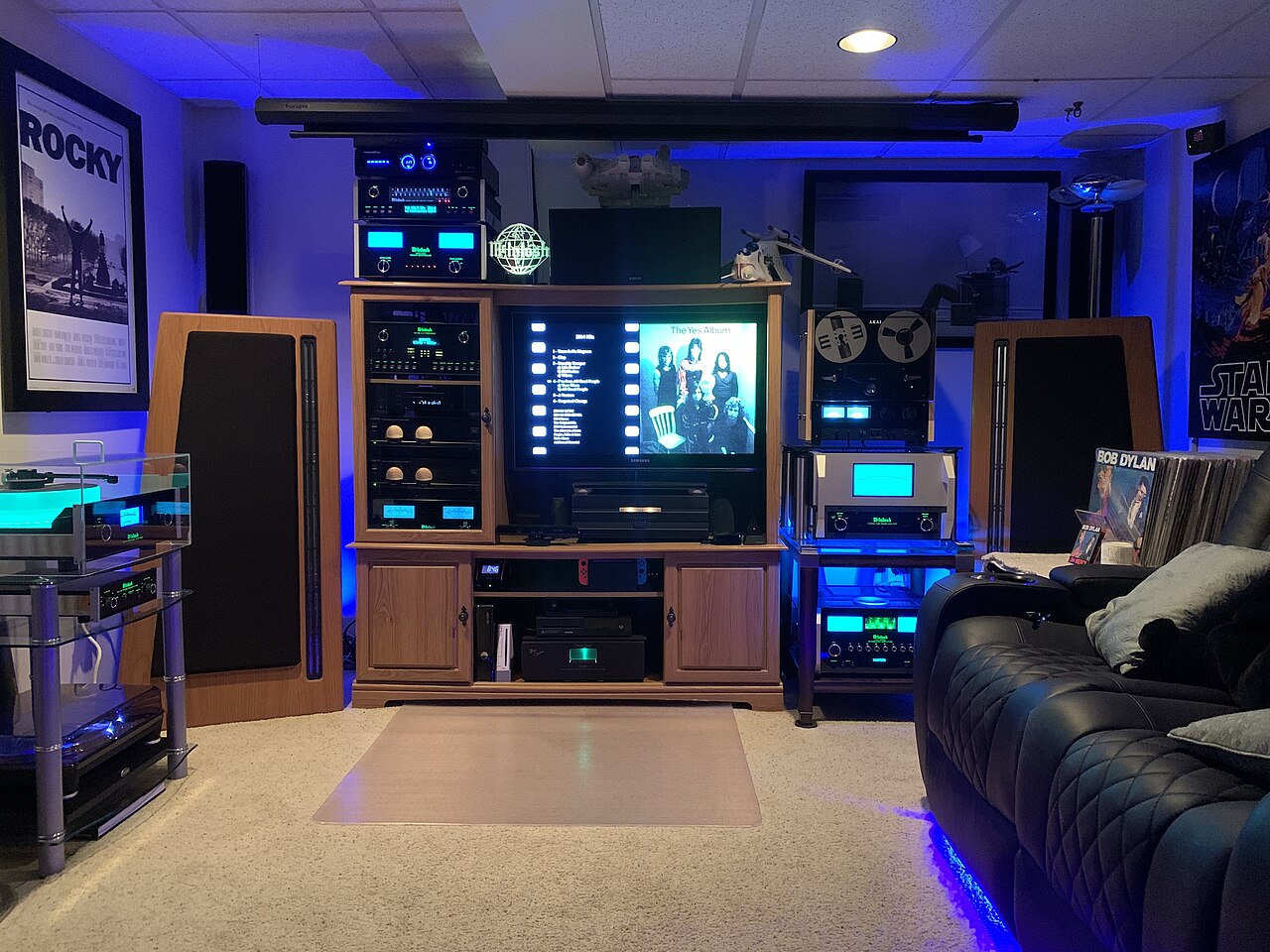 An equipment rack with amplifier level meters and floor-standing speakers either side of a display